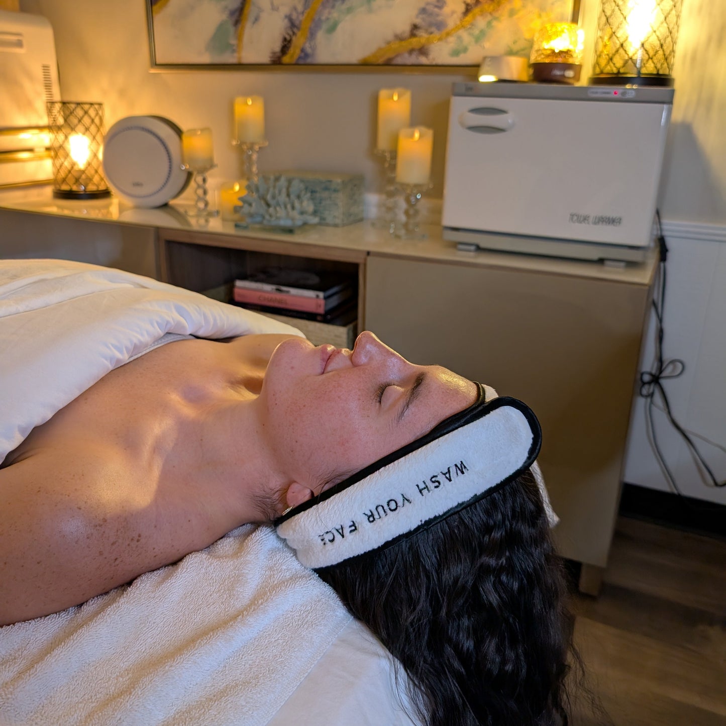 Person lying on a bed with a face mask on, in a room with candles and artwork.