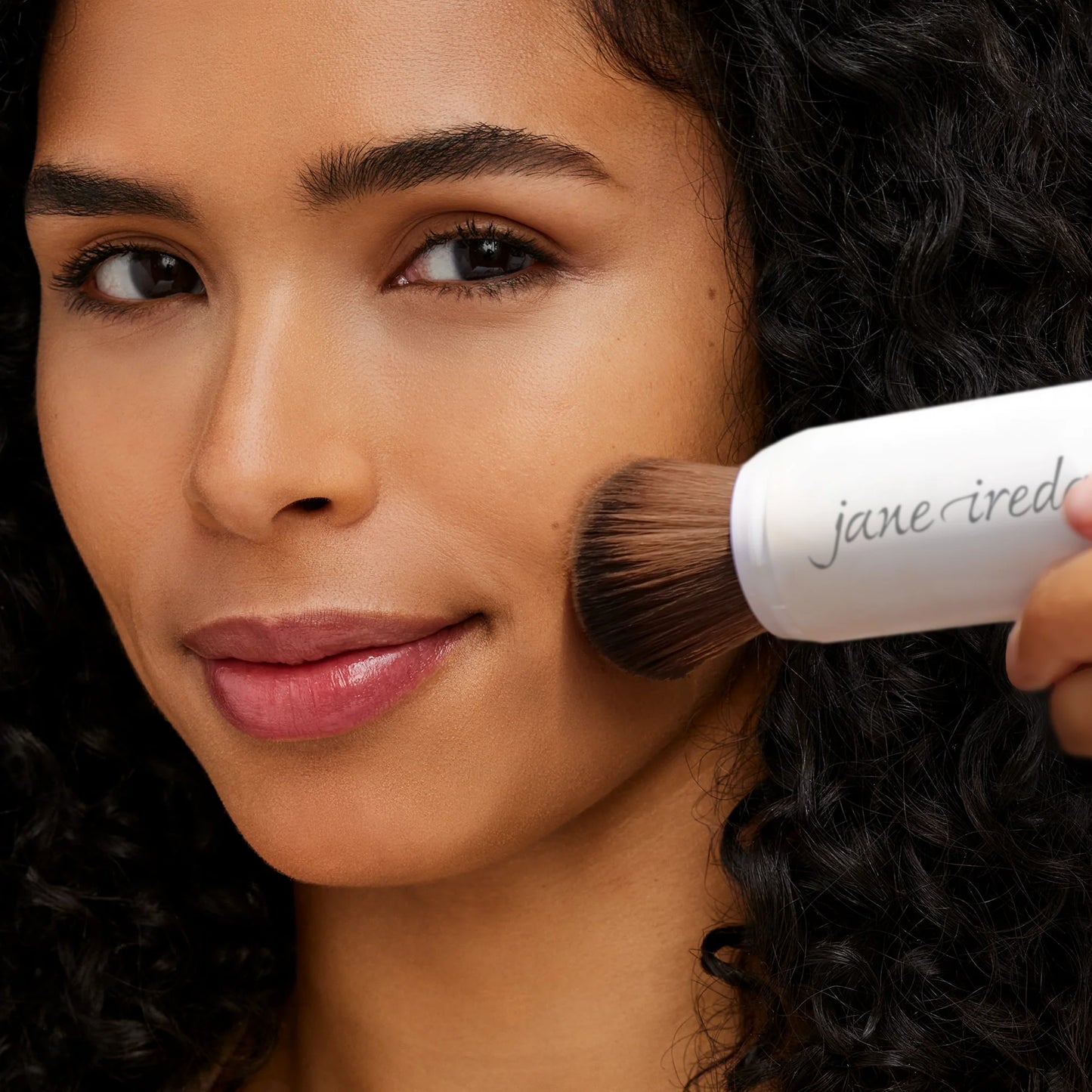 Woman applying makeup with a Jane Iredale brush to her face.