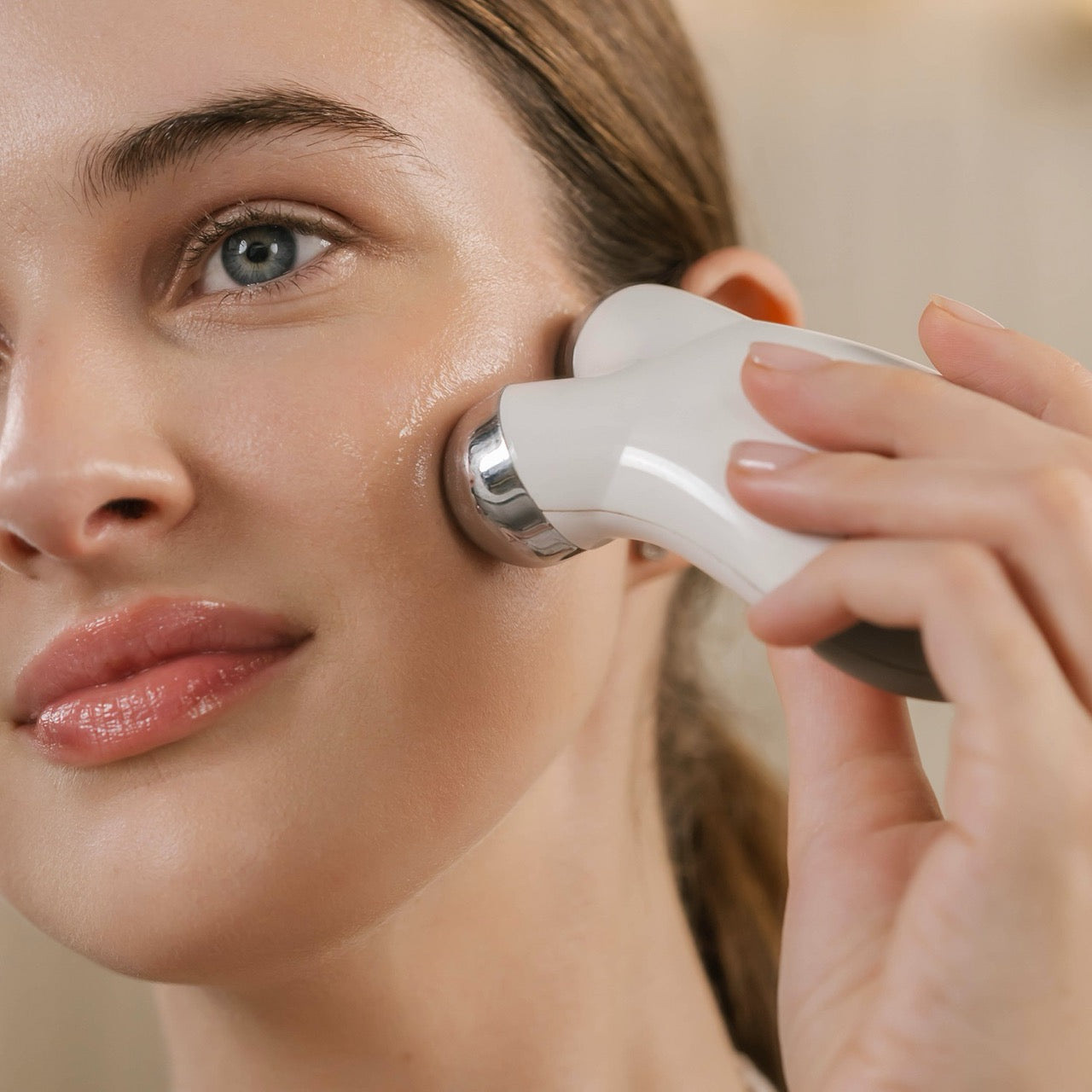 Woman gliding a handheld facial device along her cheek in Eminence Tetrapeptide Lifting Gel imagery.