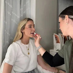 Two women applying makeup in a room with a mirror and decor.