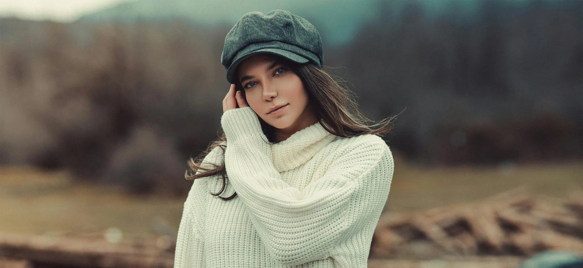 Woman wearing a white sweater and green cap standing in a field with blurred background