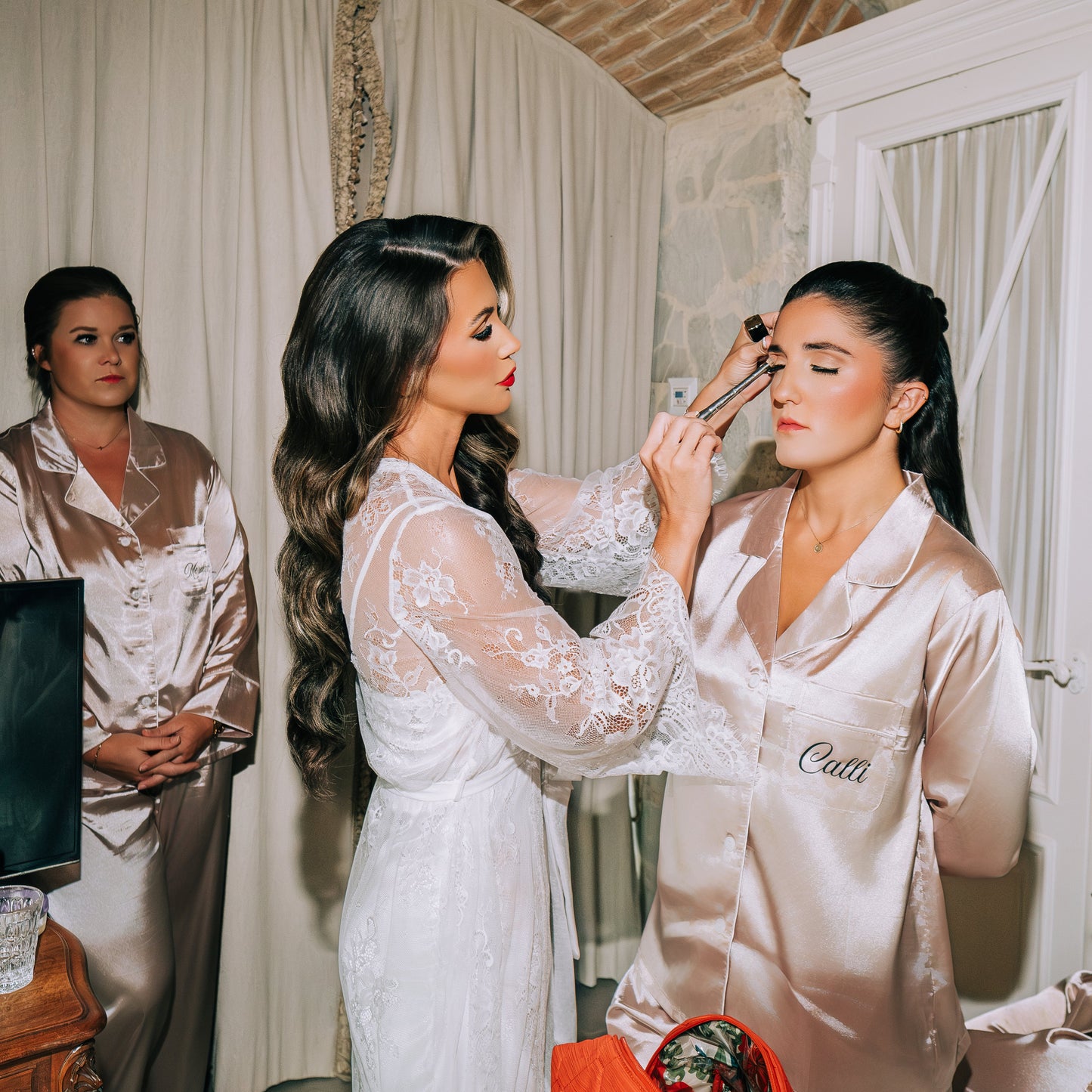 Two women getting ready in a room with a brick wall and white curtains.