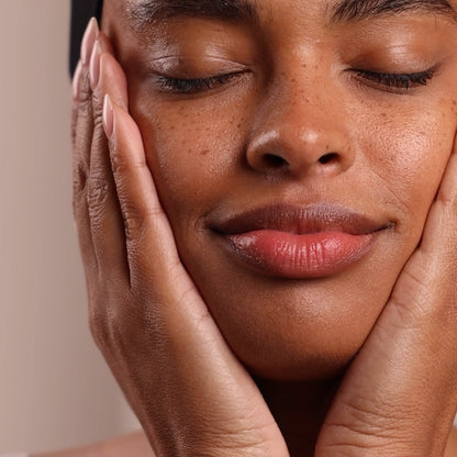 Close-up of a woman with her eyes closed, gently touching her face with her hands.