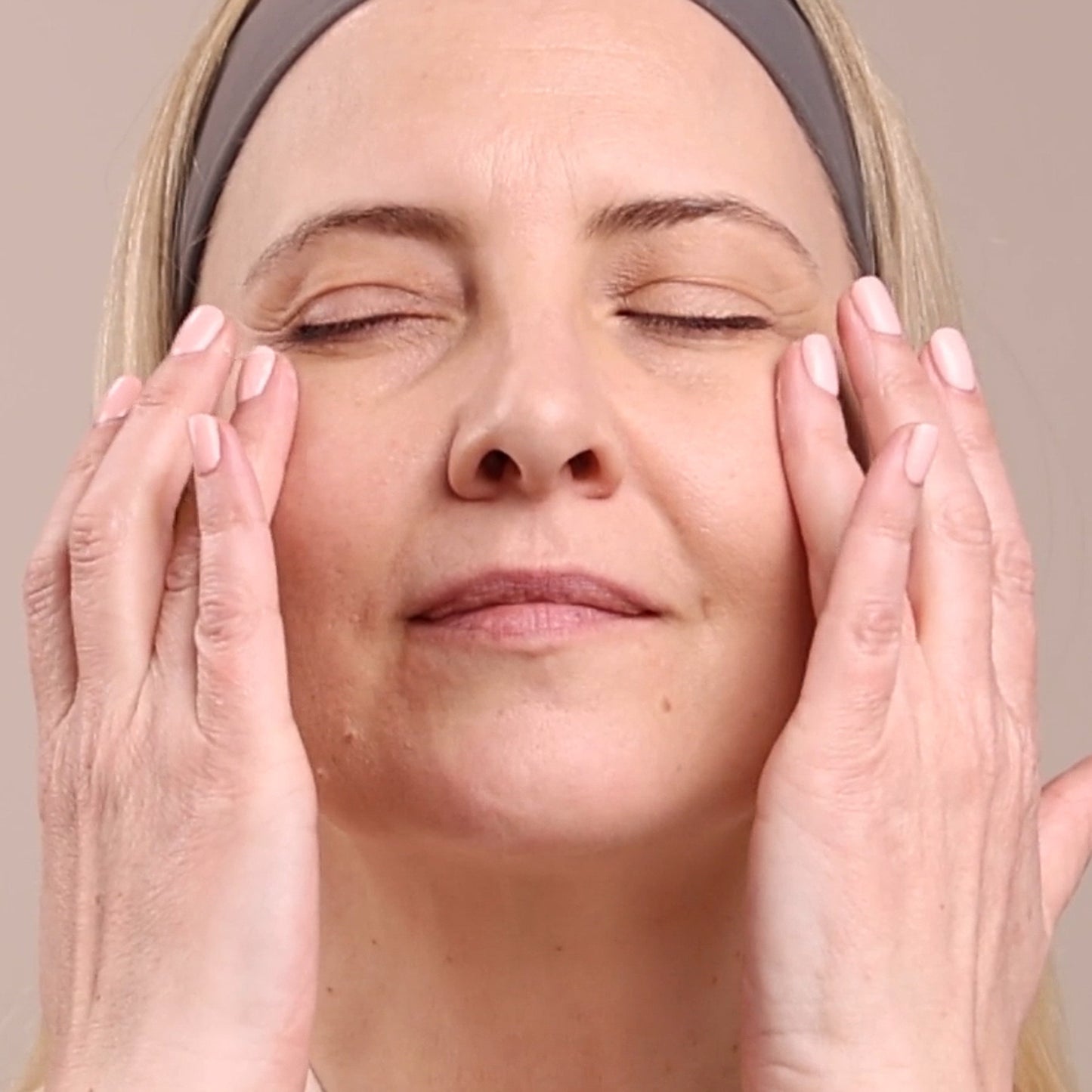 Woman applying cream to her face with a neutral background