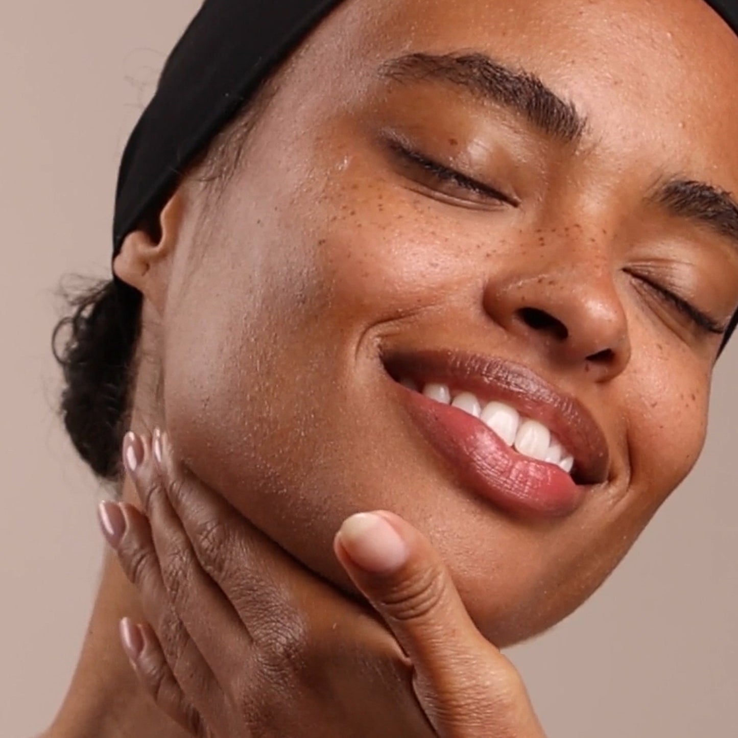 Close-up of a woman smiling with her hand on her face against a beige background