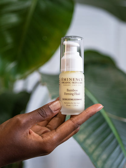 Hand holding a bottle of Eminence Bamboo Firming Fluid with green leaves in the background