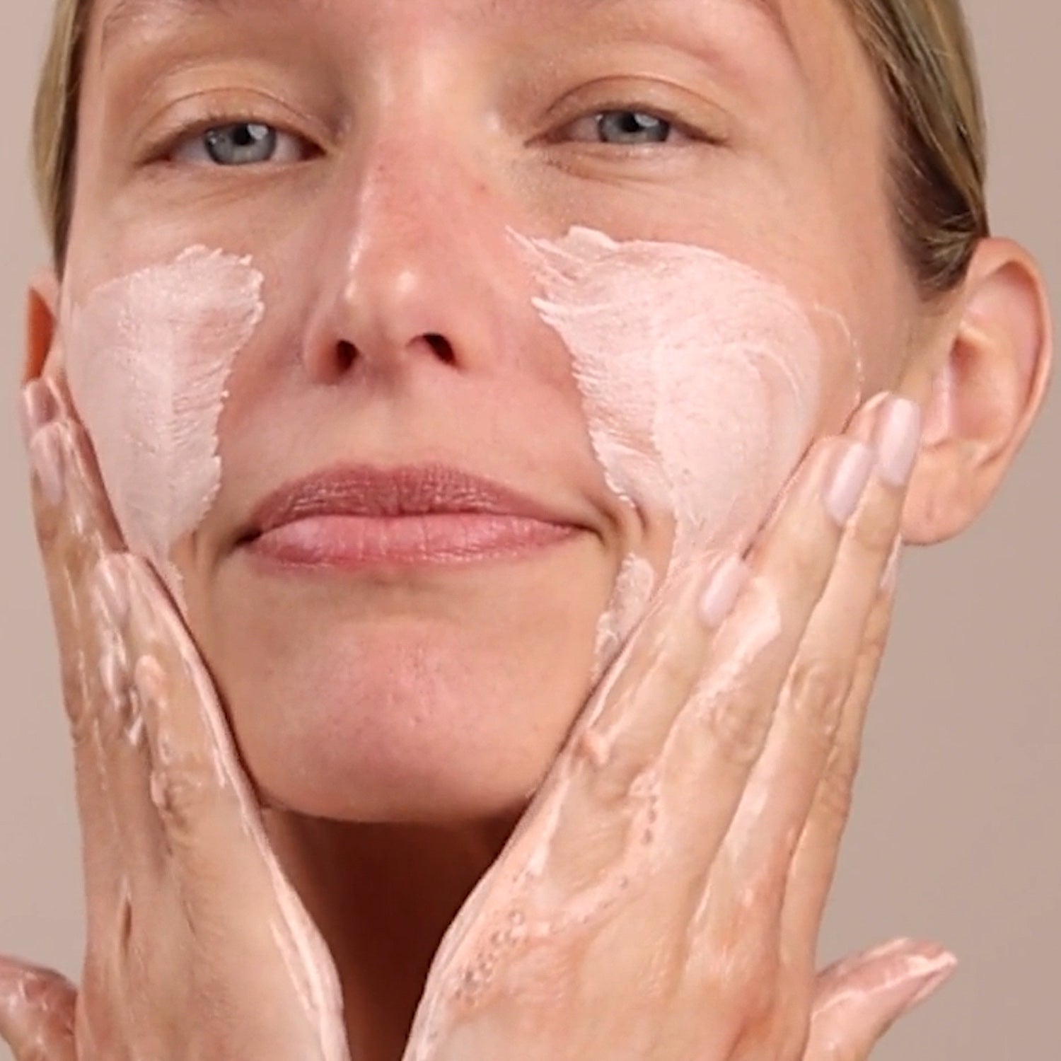 Woman applying cream to her face with a neutral background
