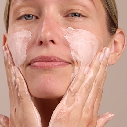 Woman applying cream to her face with a neutral background