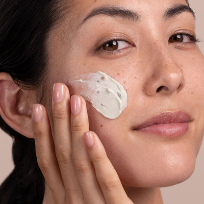 Woman applying cream to her face with a neutral background