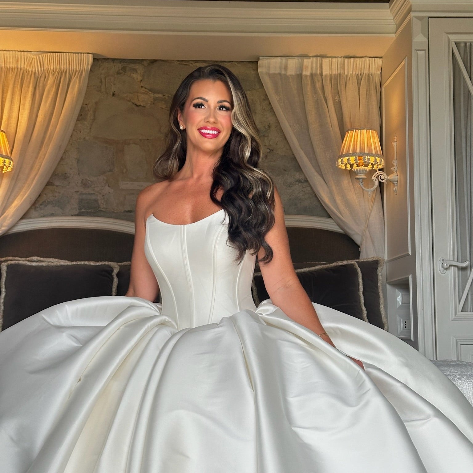 Woman in a white wedding dress sitting in a luxurious room with elegant decor.