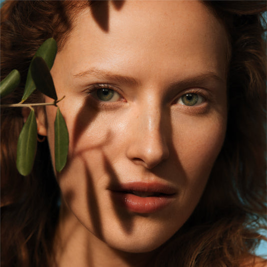 Woman with clear skin framed by olive branches, wearing Irene Forte Olive Hydrating Eye Cream