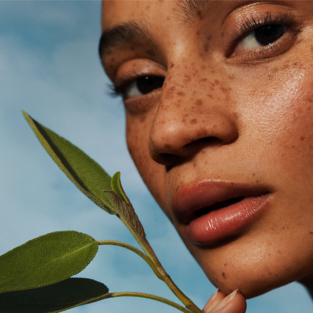 Woman with freckled skin holding a green sprig to her cheek, from Irene Forte's Pistachio Face Oil imagery