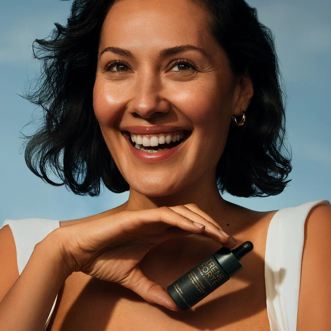 Woman holding a skincare bottle against a clear blue sky