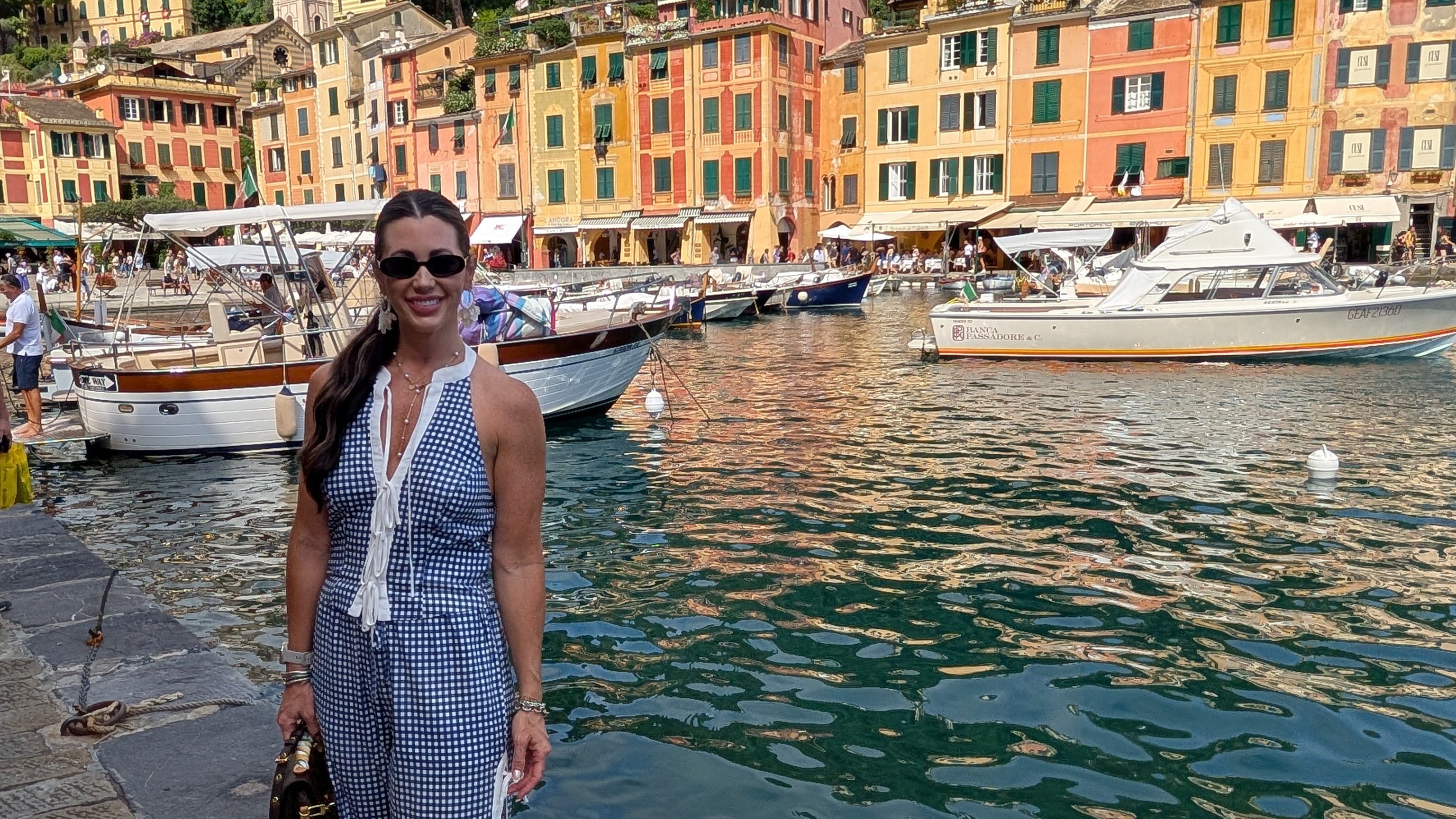 Woman in a blue checkered dress standing by a waterfront with colorful buildings in the background