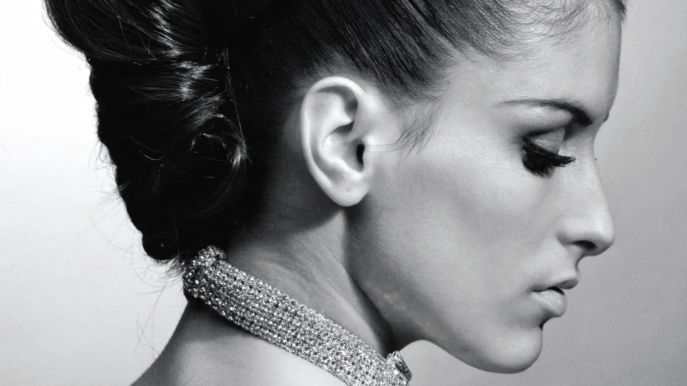 Black and white portrait of a woman with an elegant updo hairstyle and a sparkling necklace.