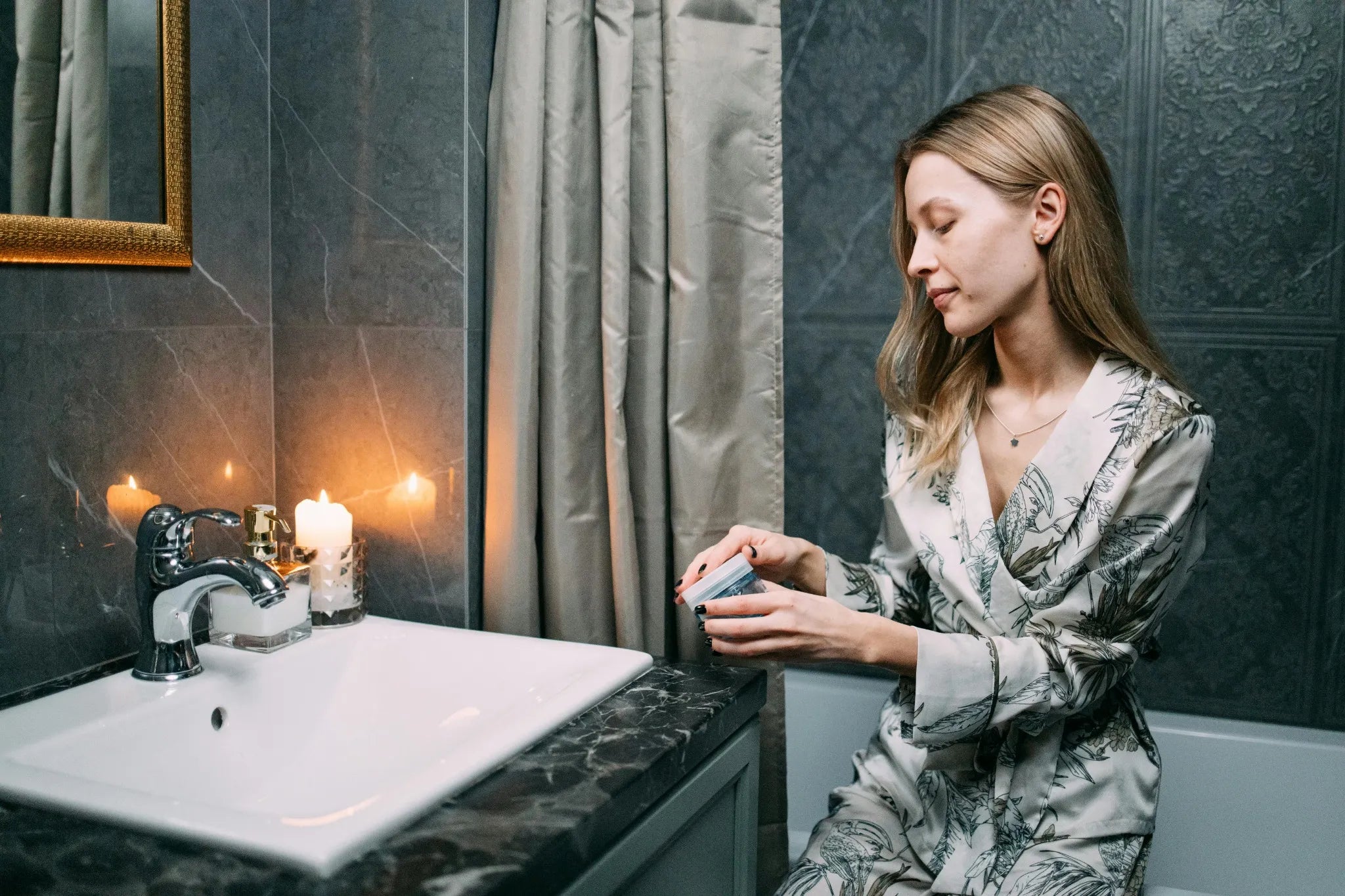 Woman applying cream in a bathroom with a sink and mirror.