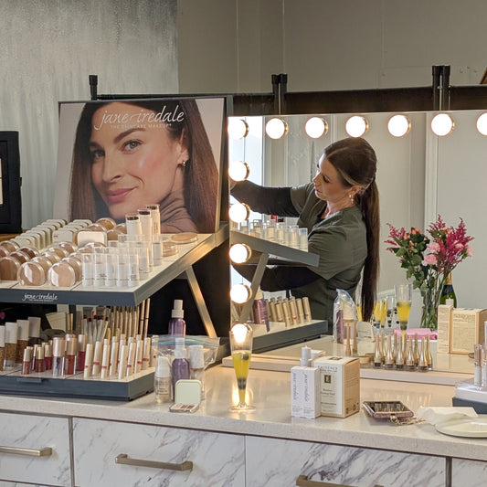 Makeup counter with various products and a woman applying makeup in a salon setting.