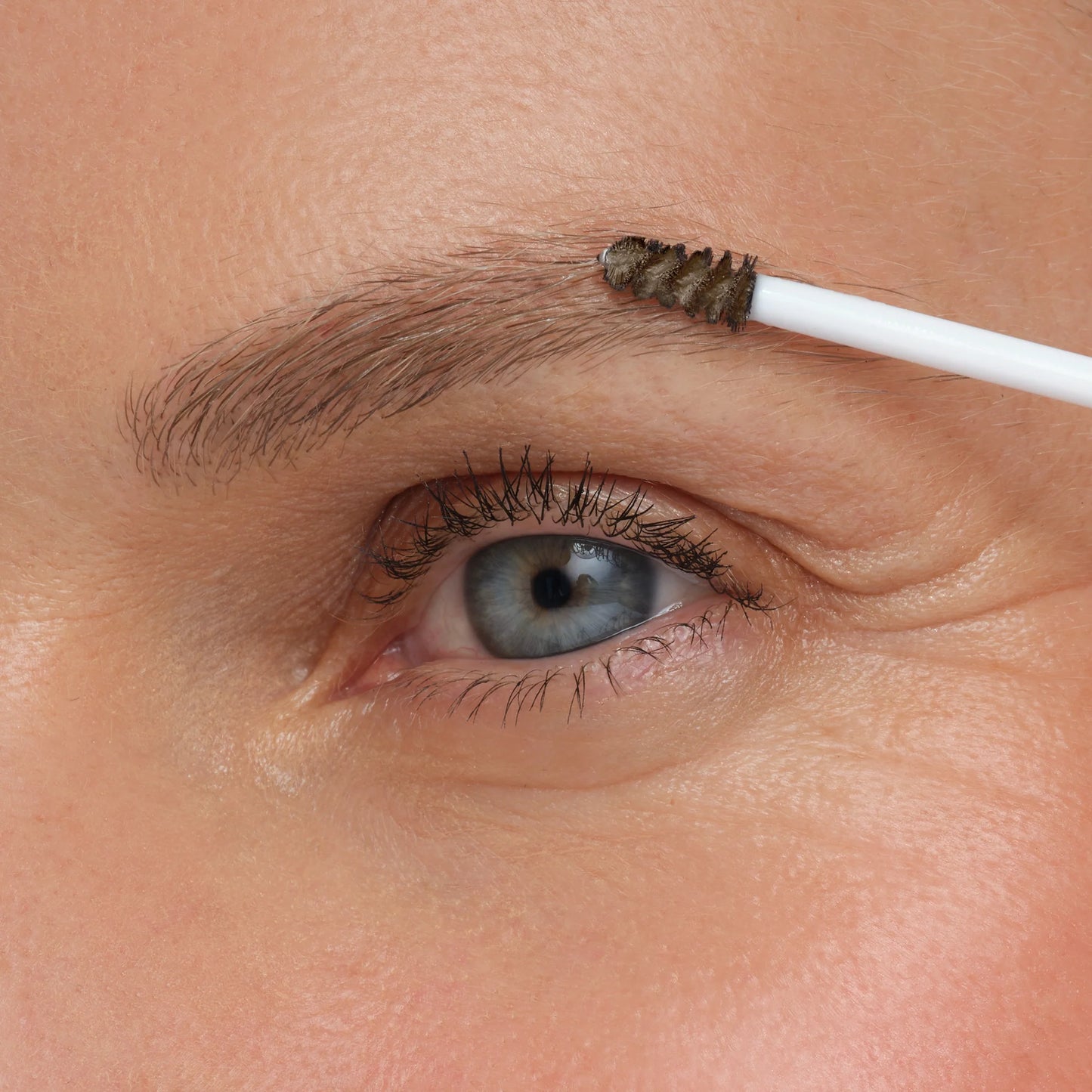 Eyebrow grooming with a small brush near an eye