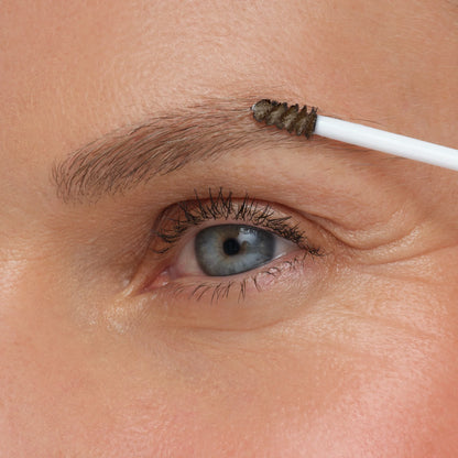Eyebrow grooming with a small brush on a close-up of an eye.