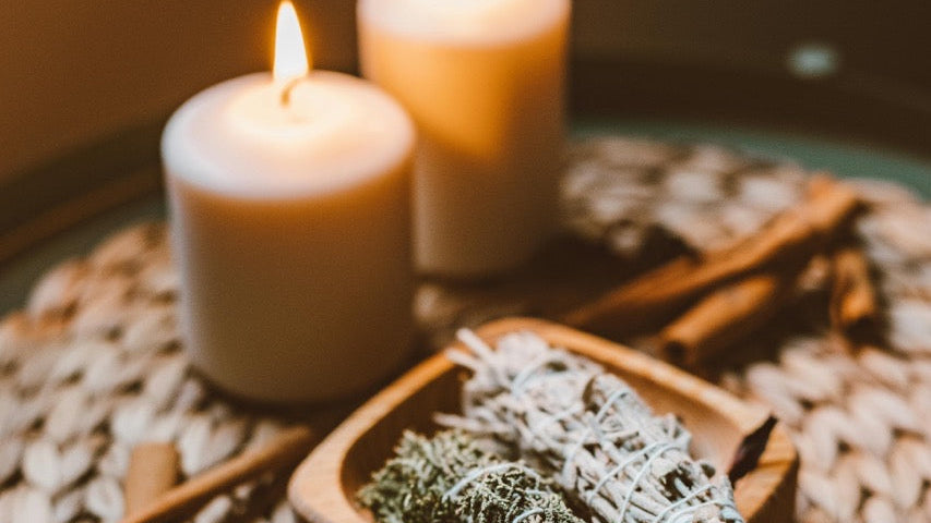 Sage smudge sticks on a woven mat with lit candles in the background