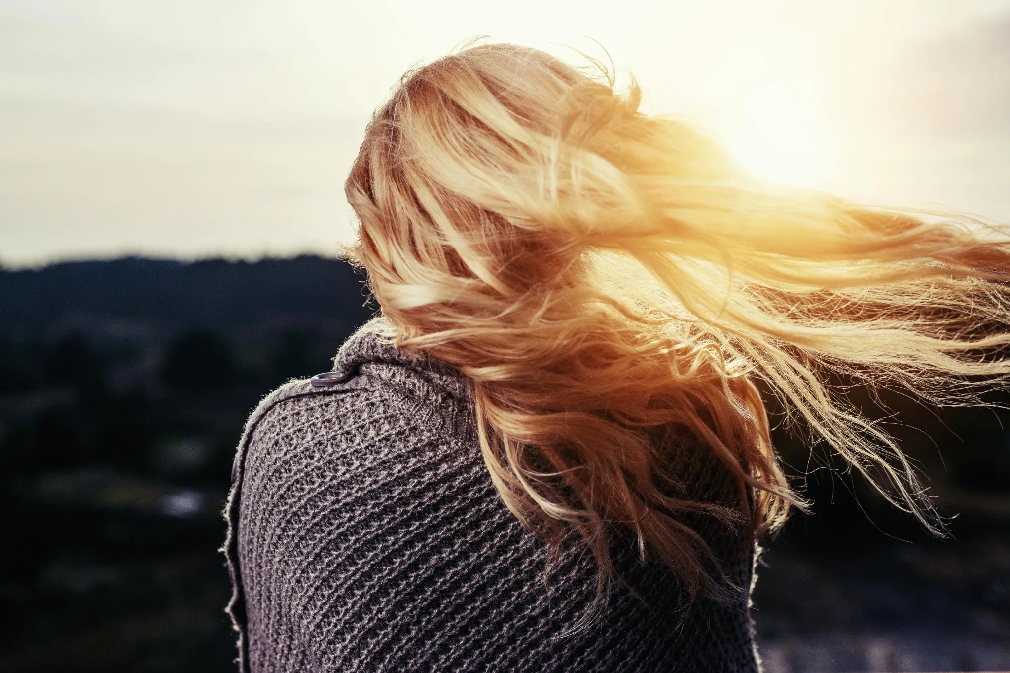 Person with blonde hair blowing in the wind against a mountainous background