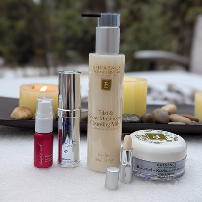 Collection of Eminence skincare products on a snowy surface with candles in the background