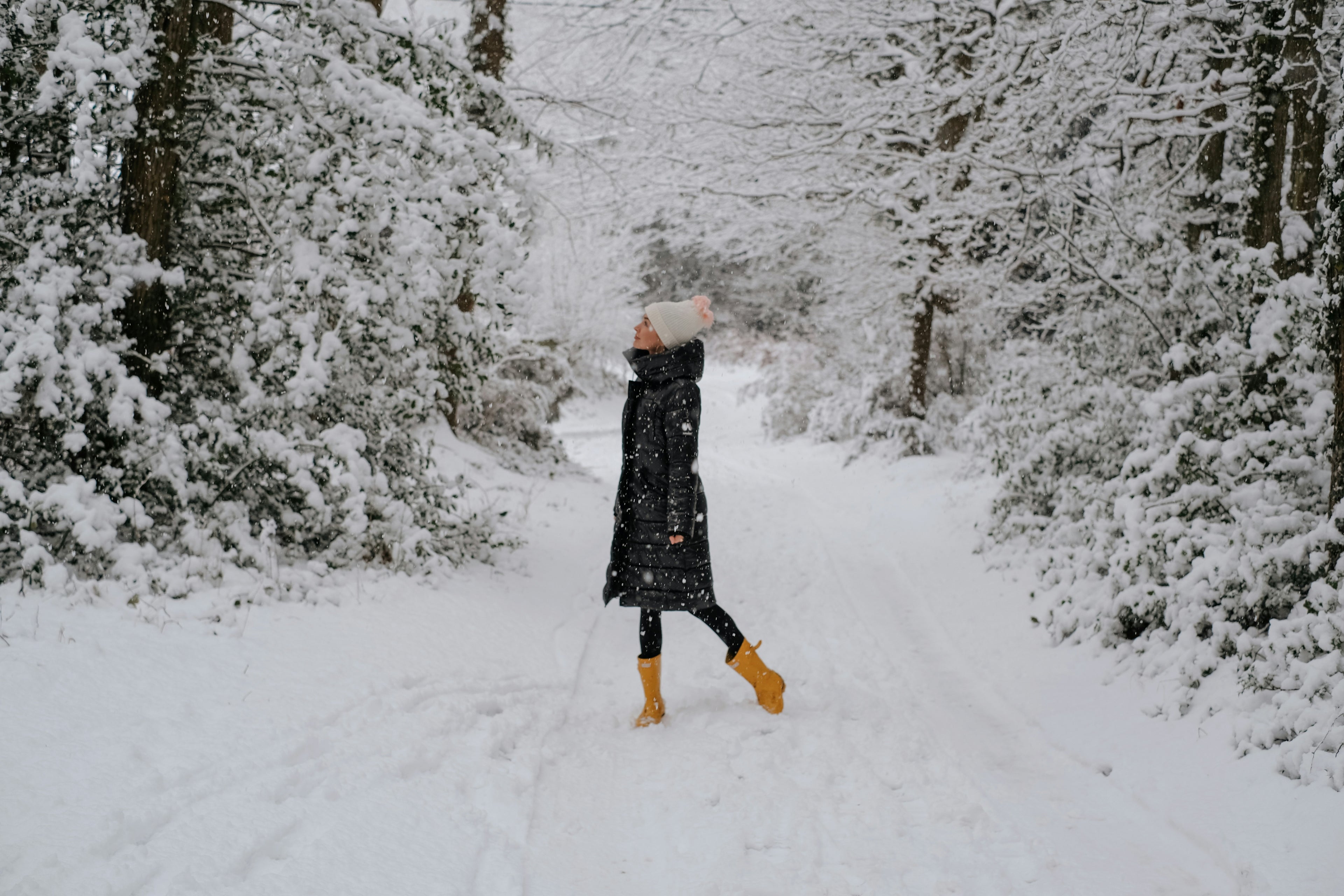 Person in a long coat and yellow boots standing in a snowy forest