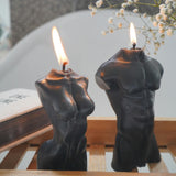 Two candle holders shaped like human figures with lit candles on a wooden surface.
