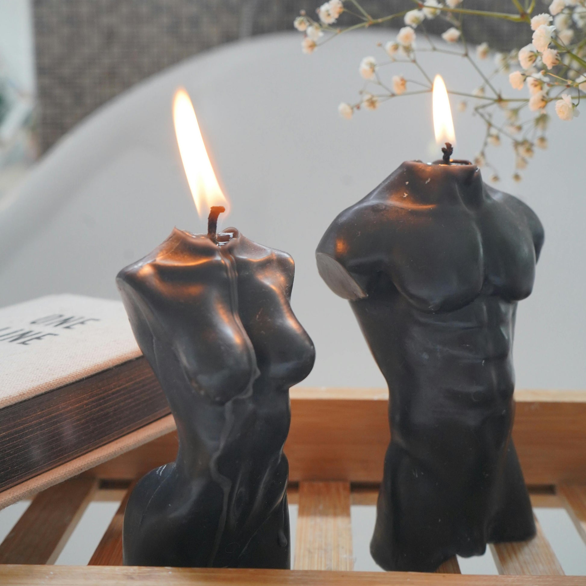 Two candle holders shaped like human figures with lit candles on a wooden surface.