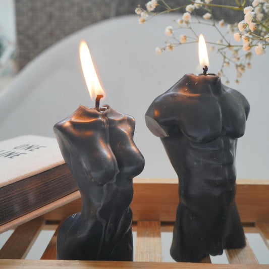 Two candle holders shaped like human figures with lit candles on a wooden surface.