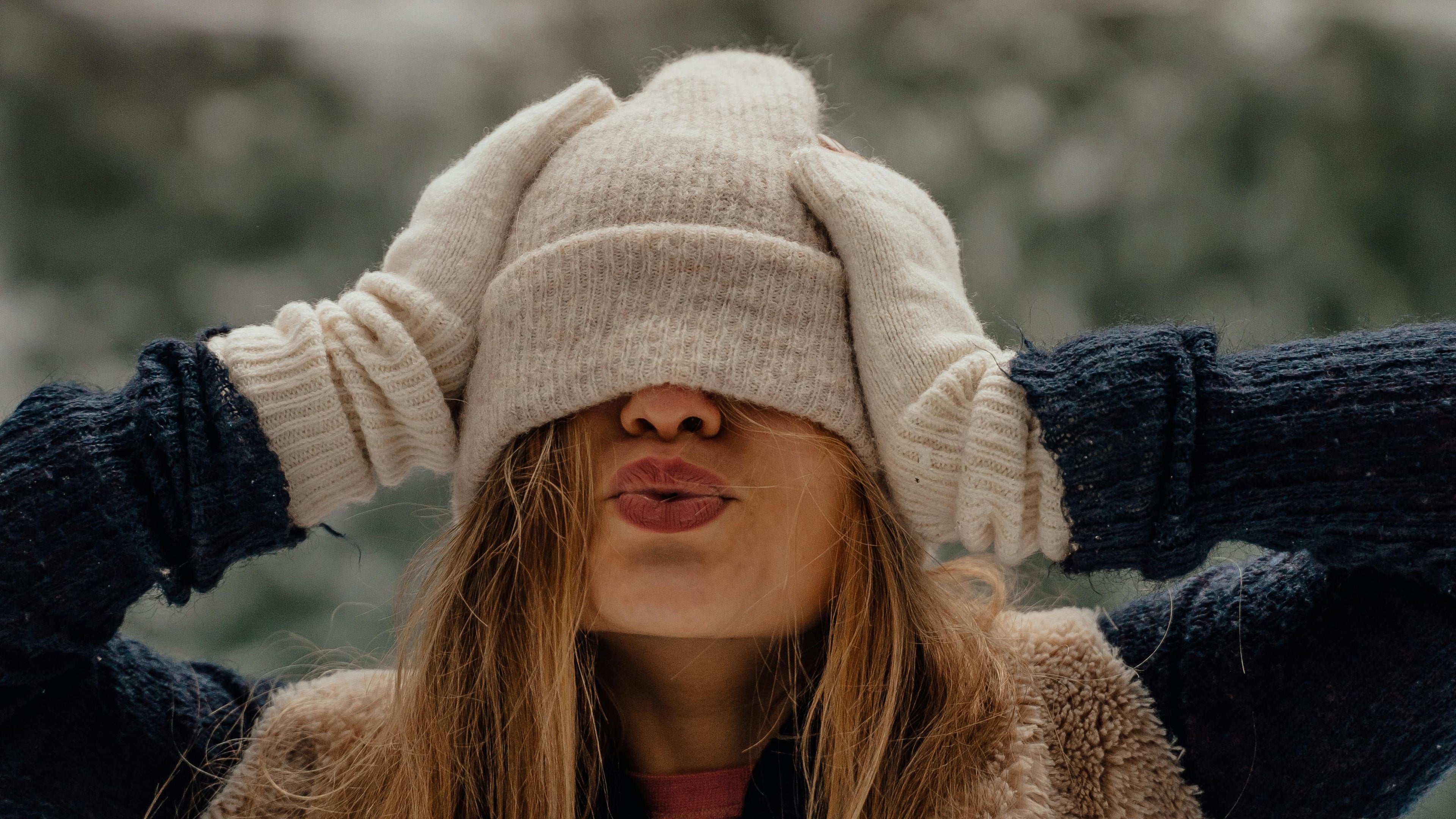 Person wearing a beige knit hat and gloves in a snowy forest