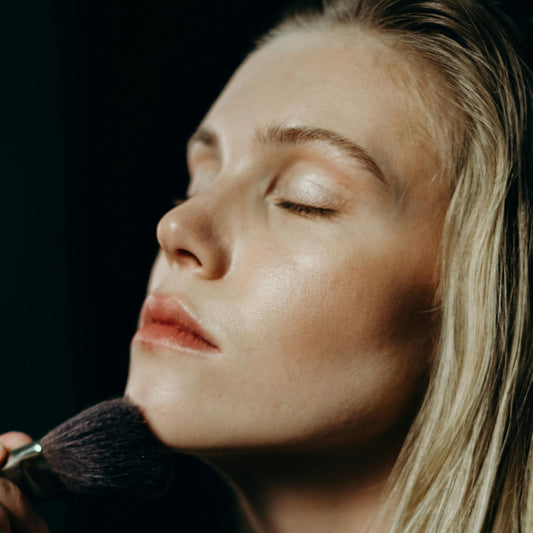 Woman applying makeup with a brush on a dark background
