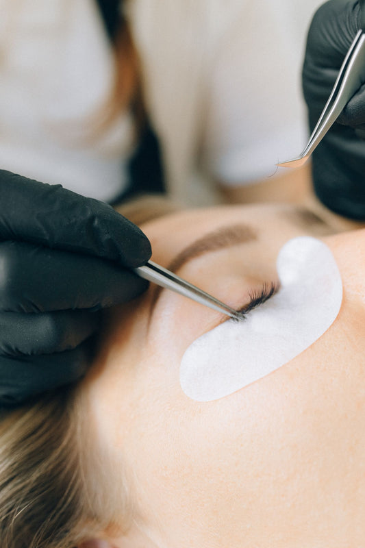 Close-up of a lash lift and tint treatment, with a lash tool and a white under-eye pad in place.