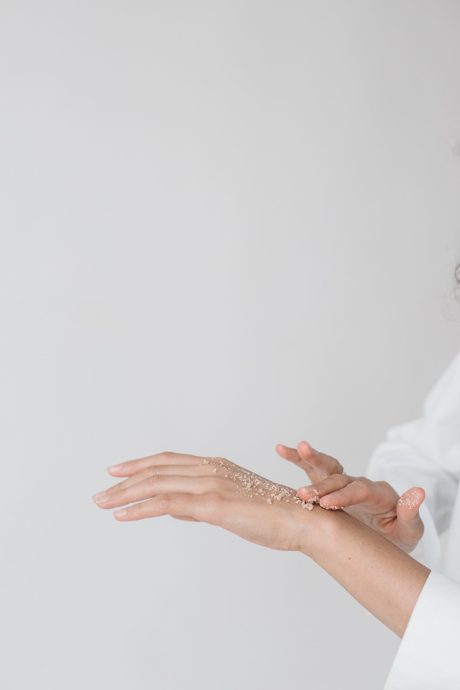 Hands being treated with a fine exfoliating scrub, dusted across the skin against a pale backdrop.