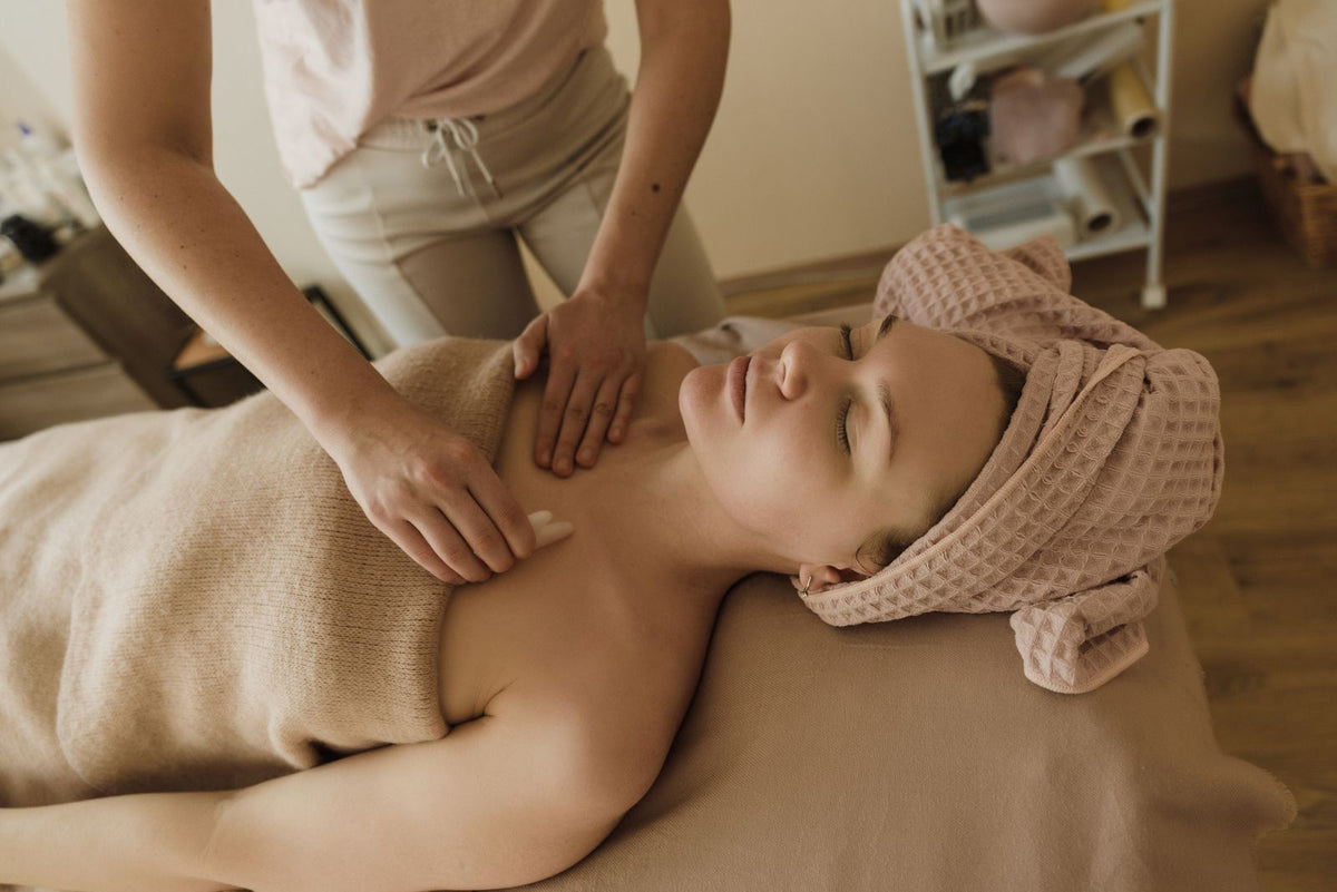 Therapist's hands working across the shoulders and chest of a client resting on a spa bed.