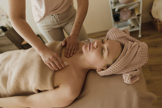 Therapist's hands working across the shoulders and chest of a client resting on a spa bed.