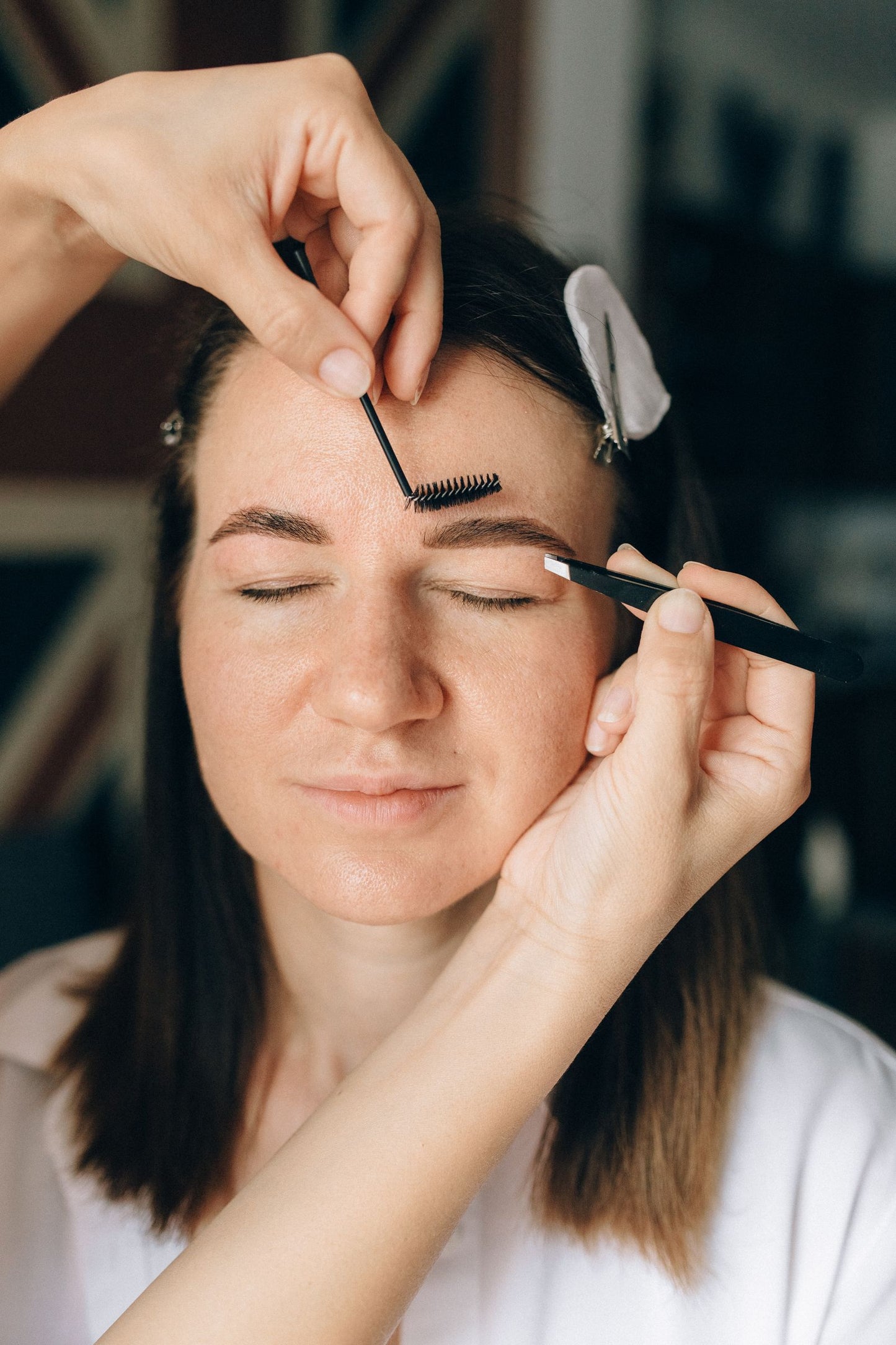 Brow lamination in progress: brows brushed upward with a spoolie while the client rests with eyes closed.