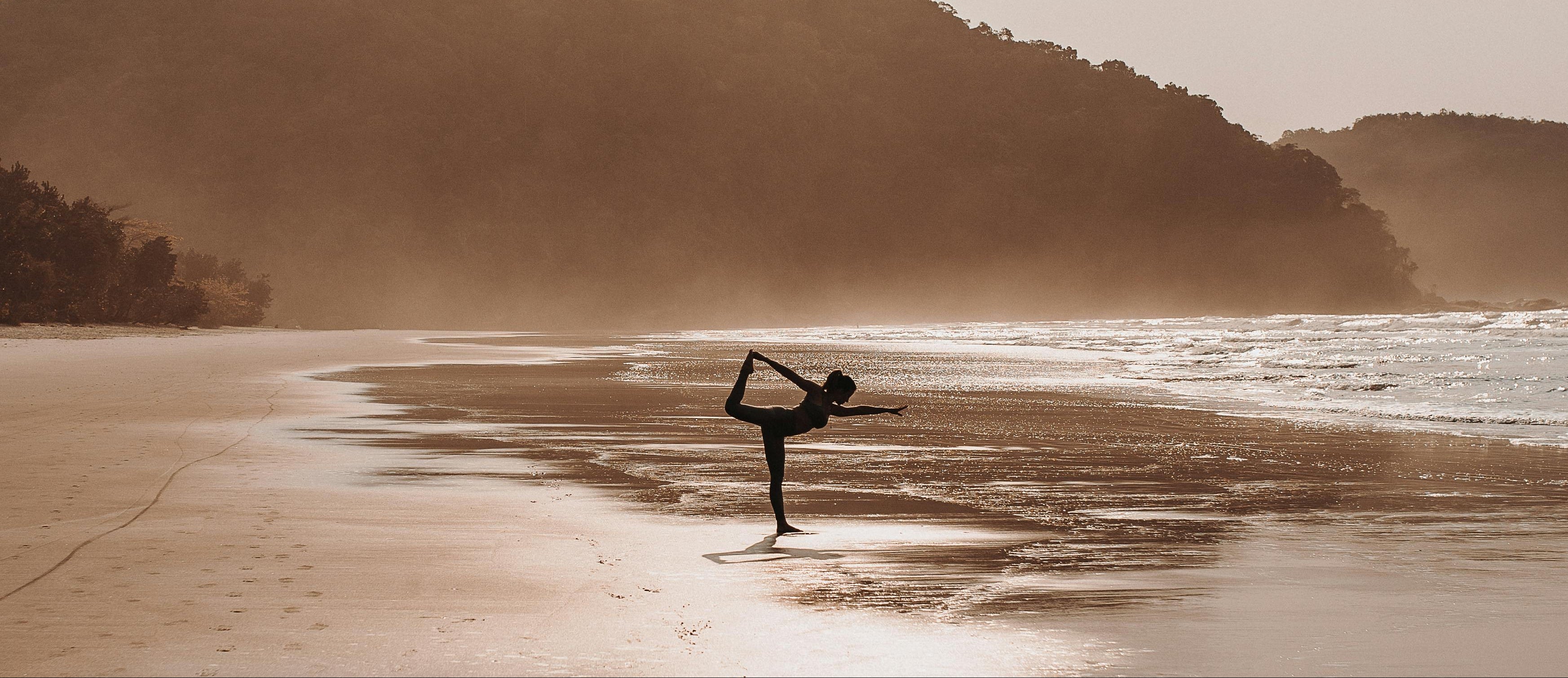 Person practicing yoga on a beach with a mountain in the background