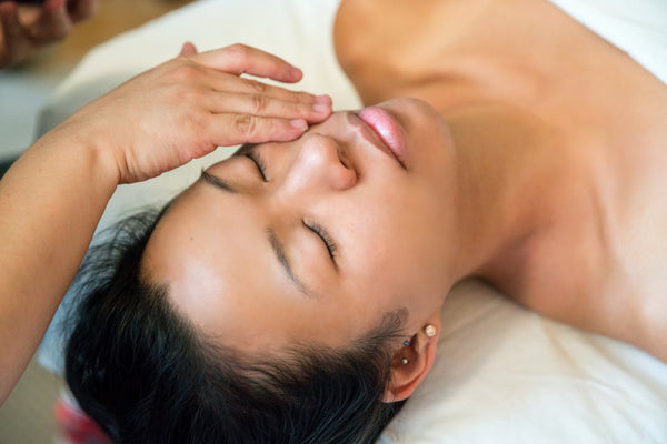 Two hands resting across the forehead and eyes of a woman lying back on a treatment bed.